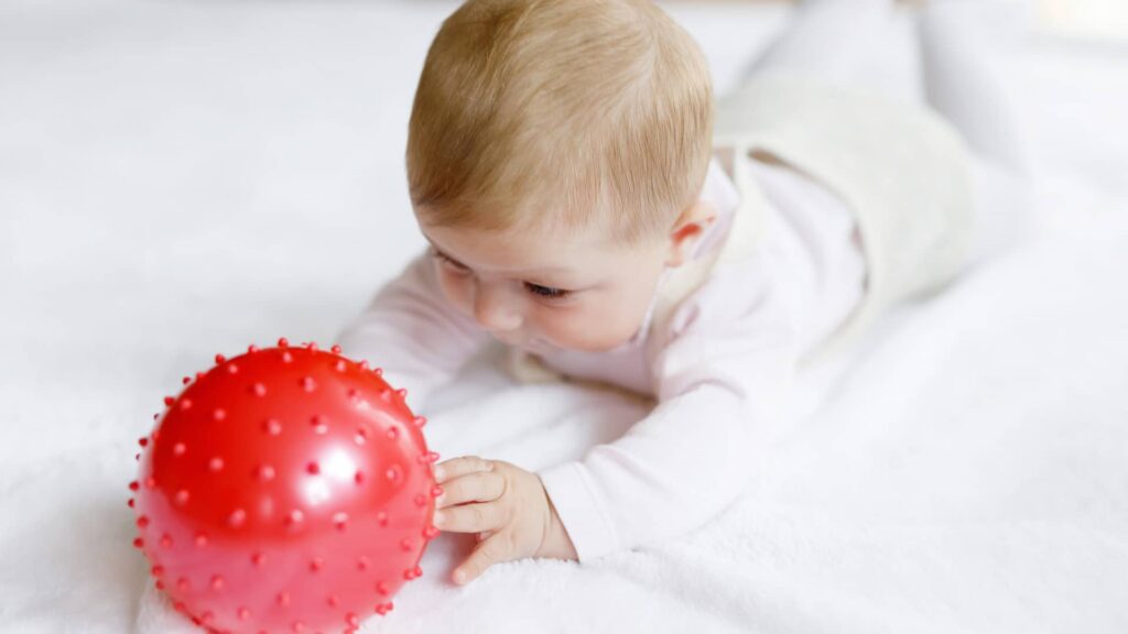 ein Kleinkind liegt auf einer Matte und spielt mit einem Ball